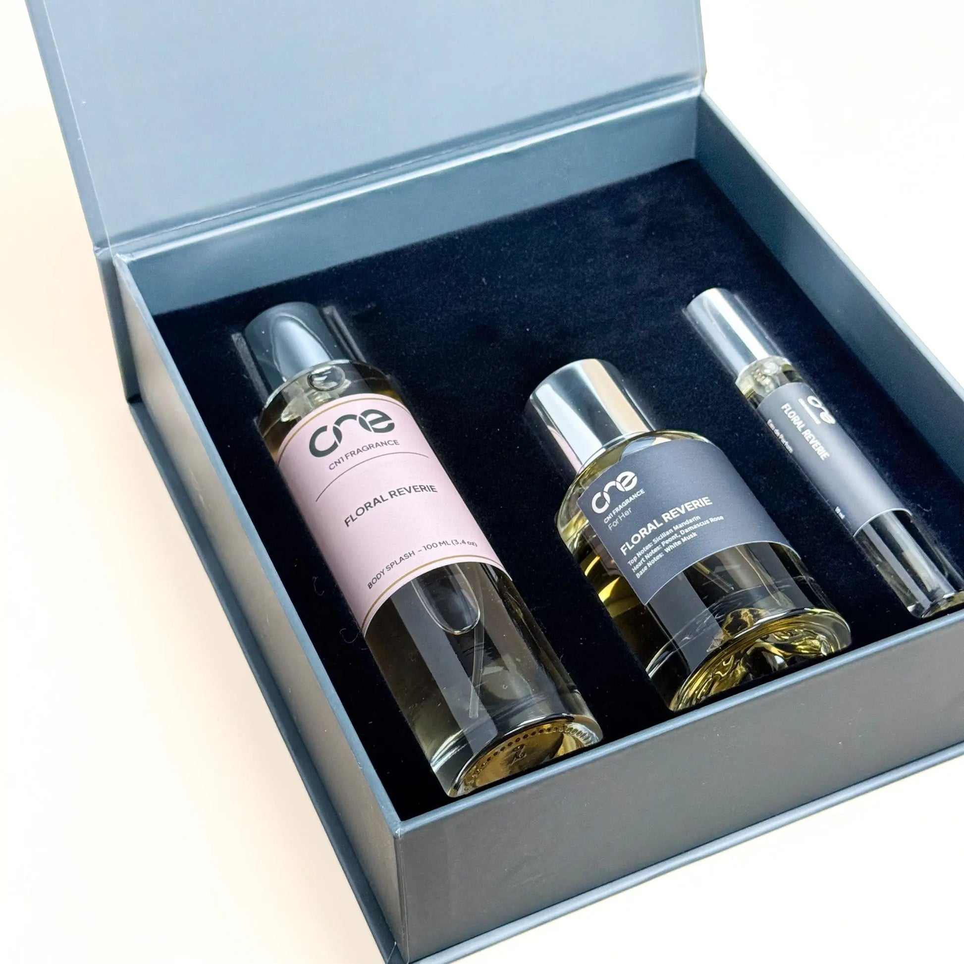 Two perfume bottles and a spray device in an open box on a light beige background
