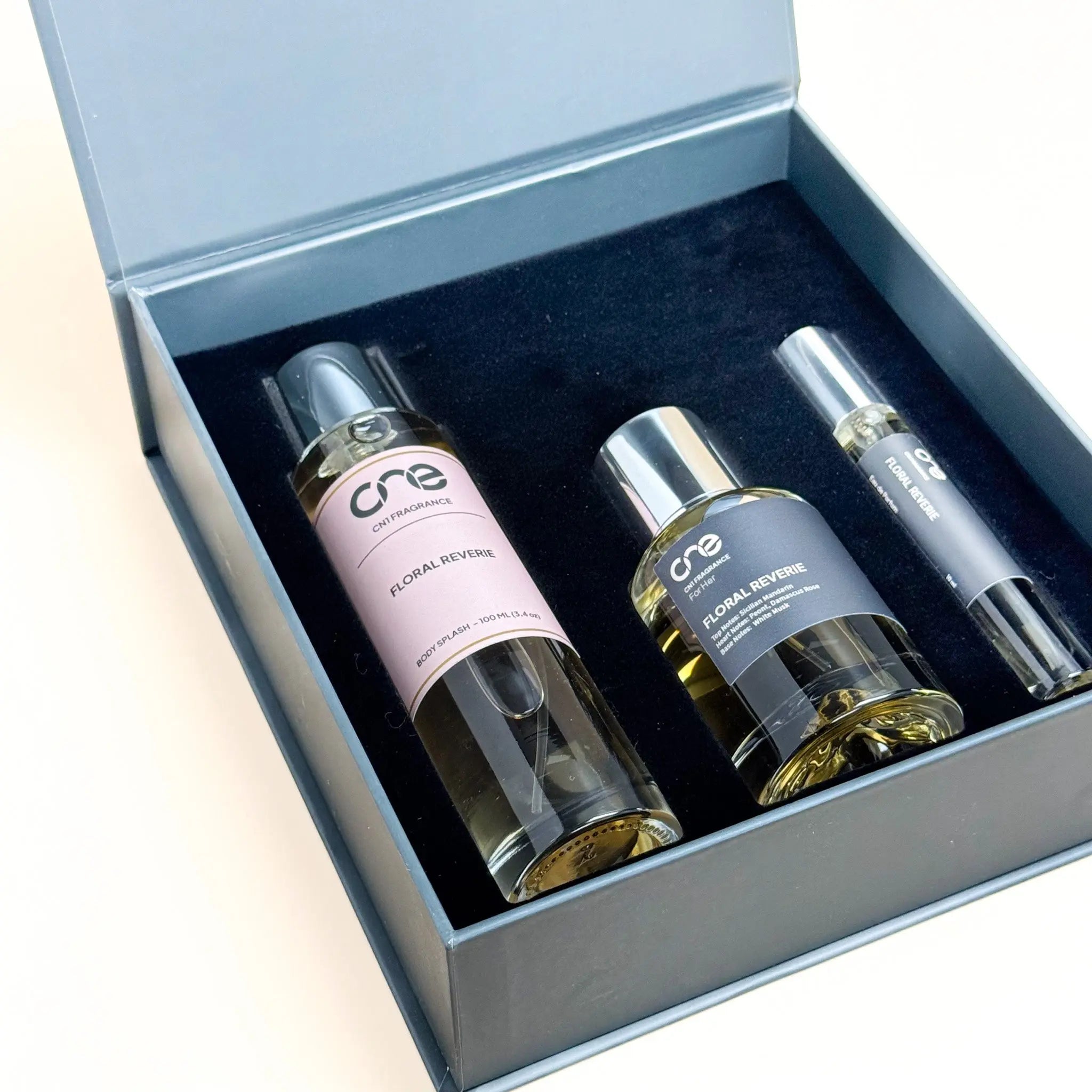 Two perfume bottles and a spray device in an open box on a light beige background